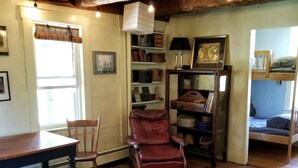 A rustic living room with wooden floors, a leather armchair, a sofa, a wooden coffee table, and a bookshelf.