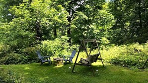 A grassy outdoor area with a swing set, two Adirondack chairs, and a small wooden table.