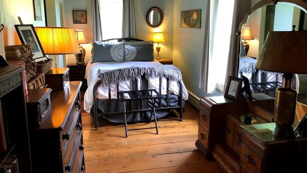 A cozy bedroom with a bed, wooden dresser, and a desk with a lamp.