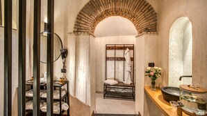 Un baño con un arco de piedra, un tocador con lavamanos y un perchero para toallas.