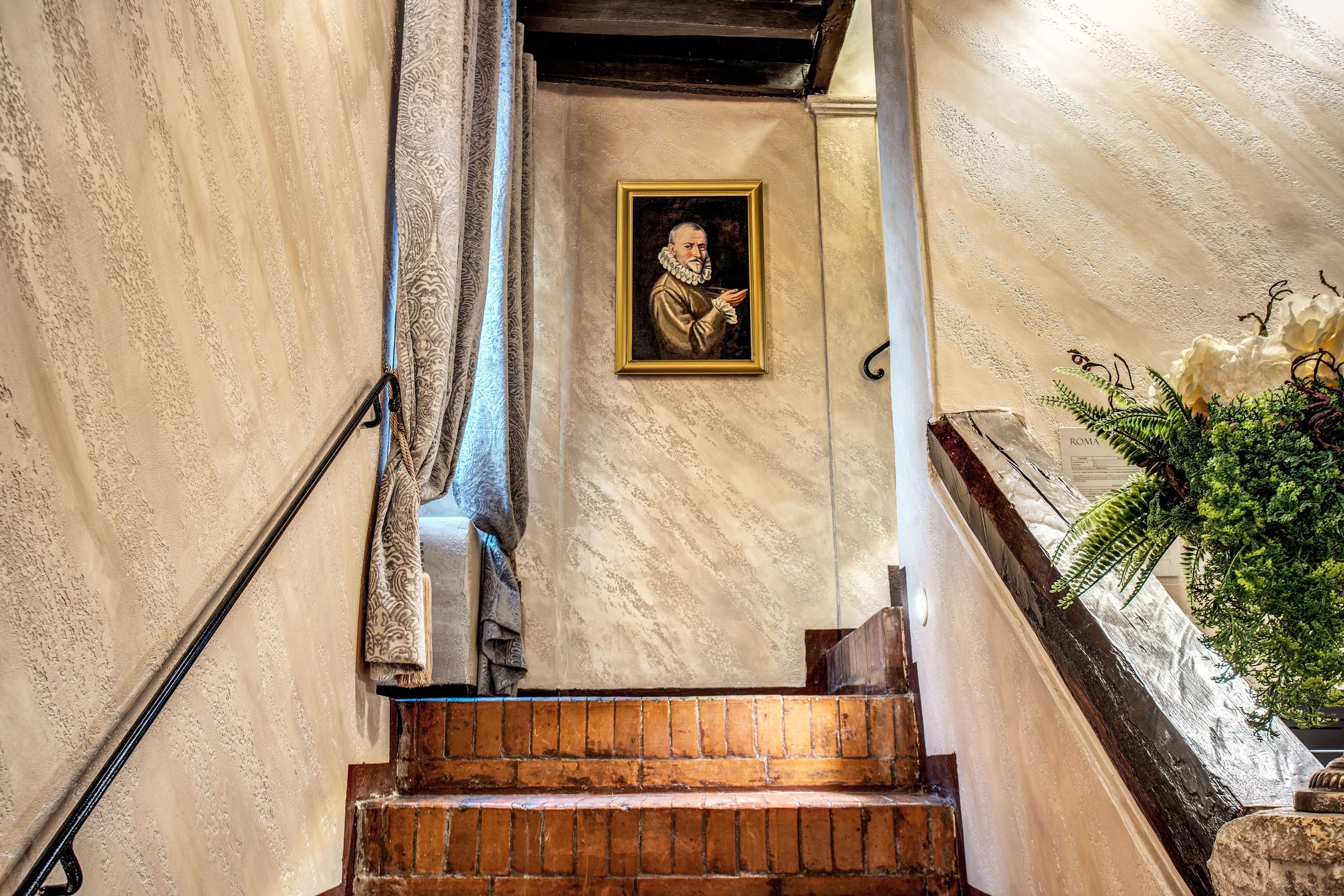 A staircase with a framed portrait on the wall, a potted plant, and a textured wall.
