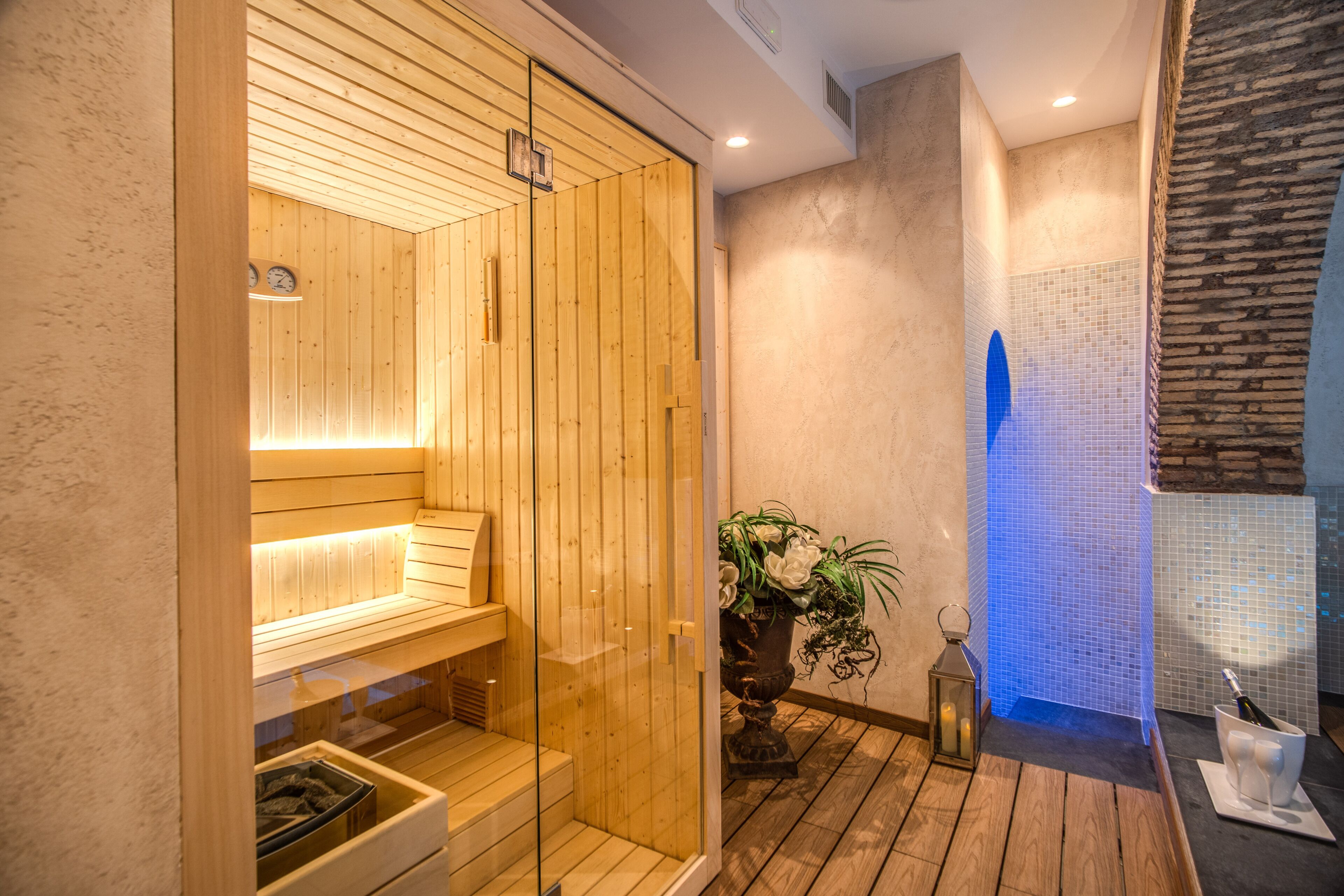 A sauna with wooden walls and a glass door, a potted plant, and a small table with a candle and a glass.