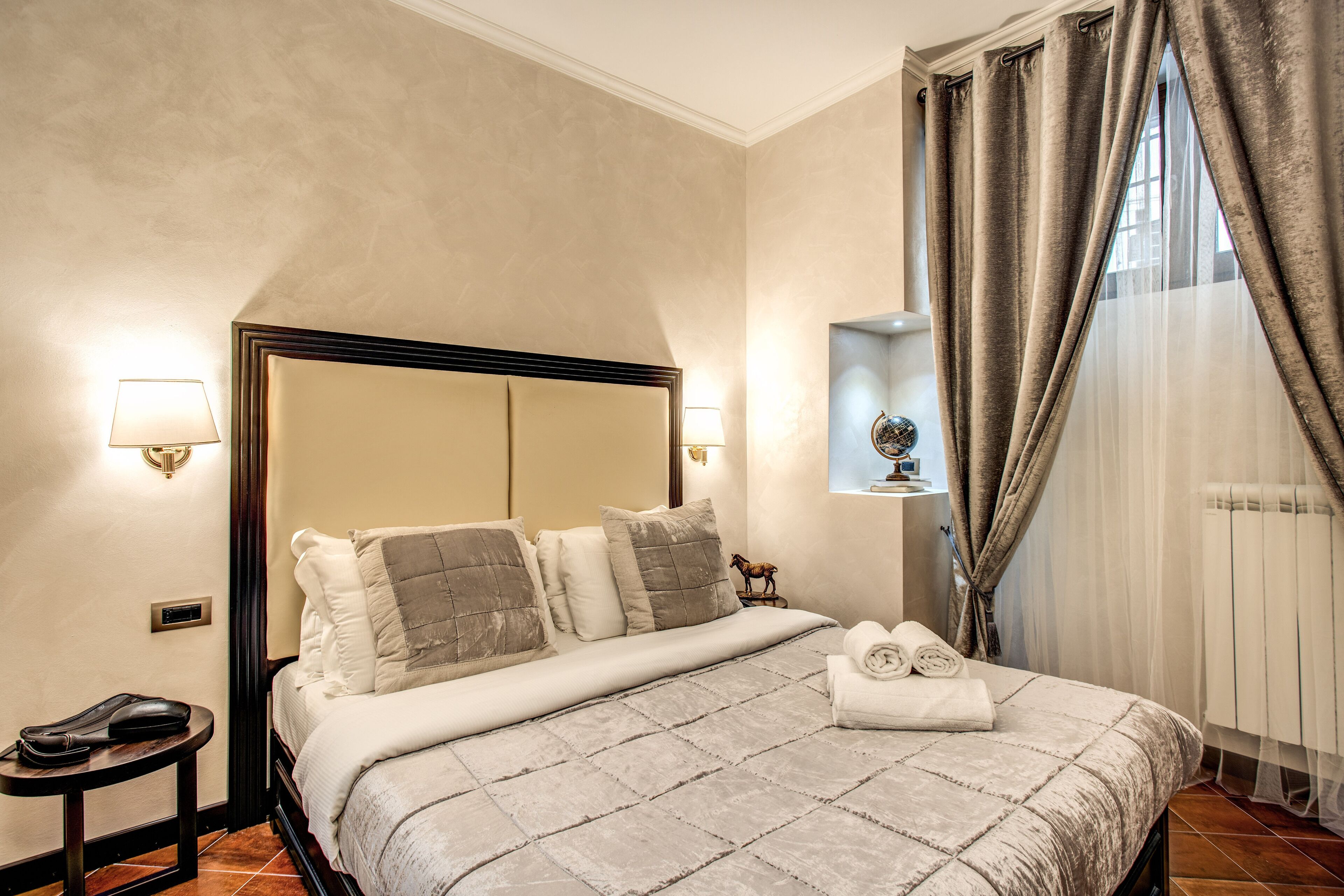 A hotel room with a large bed, a nightstand, a lamp, and a window with curtains.