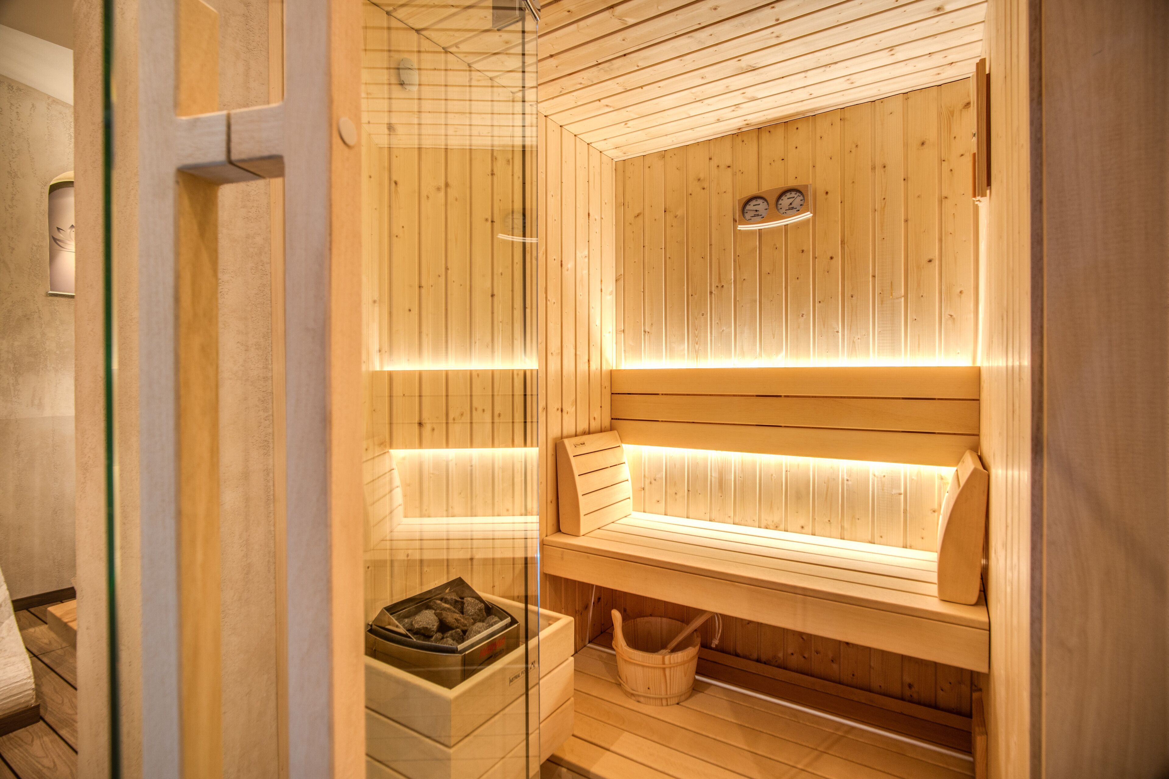 Una sauna in legno con panche, una porta in vetro e una panca con un cesto sottostante.