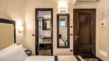 A hotel room with a bed, bedside lamp, a mirror, a door, and a wall-mounted air conditioning unit.