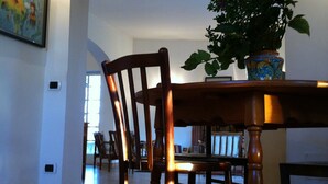 Uma sala de jantar com uma mesa e cadeiras de madeira, uma planta em vaso e um quadro na parede.