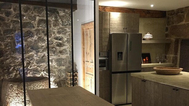 Una cocina moderna con pared de piedra, armarios de madera y un refrigerador de acero inoxidable.