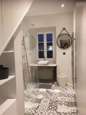 A narrow bathroom with a white sink, a mirror, and patterned floor tiles.