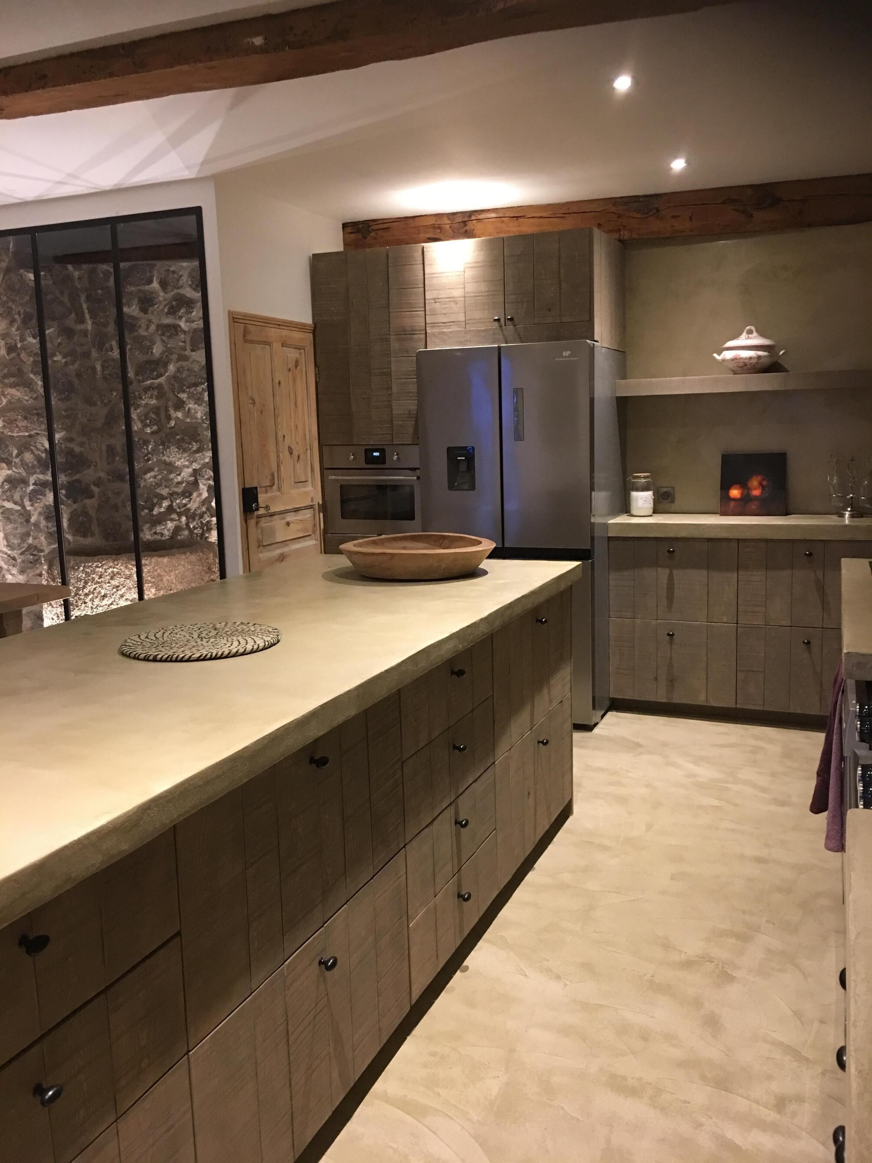 Une cuisine moderne avec des meubles en bois, un grand îlot central, un four encastré et un réfrigérateur.