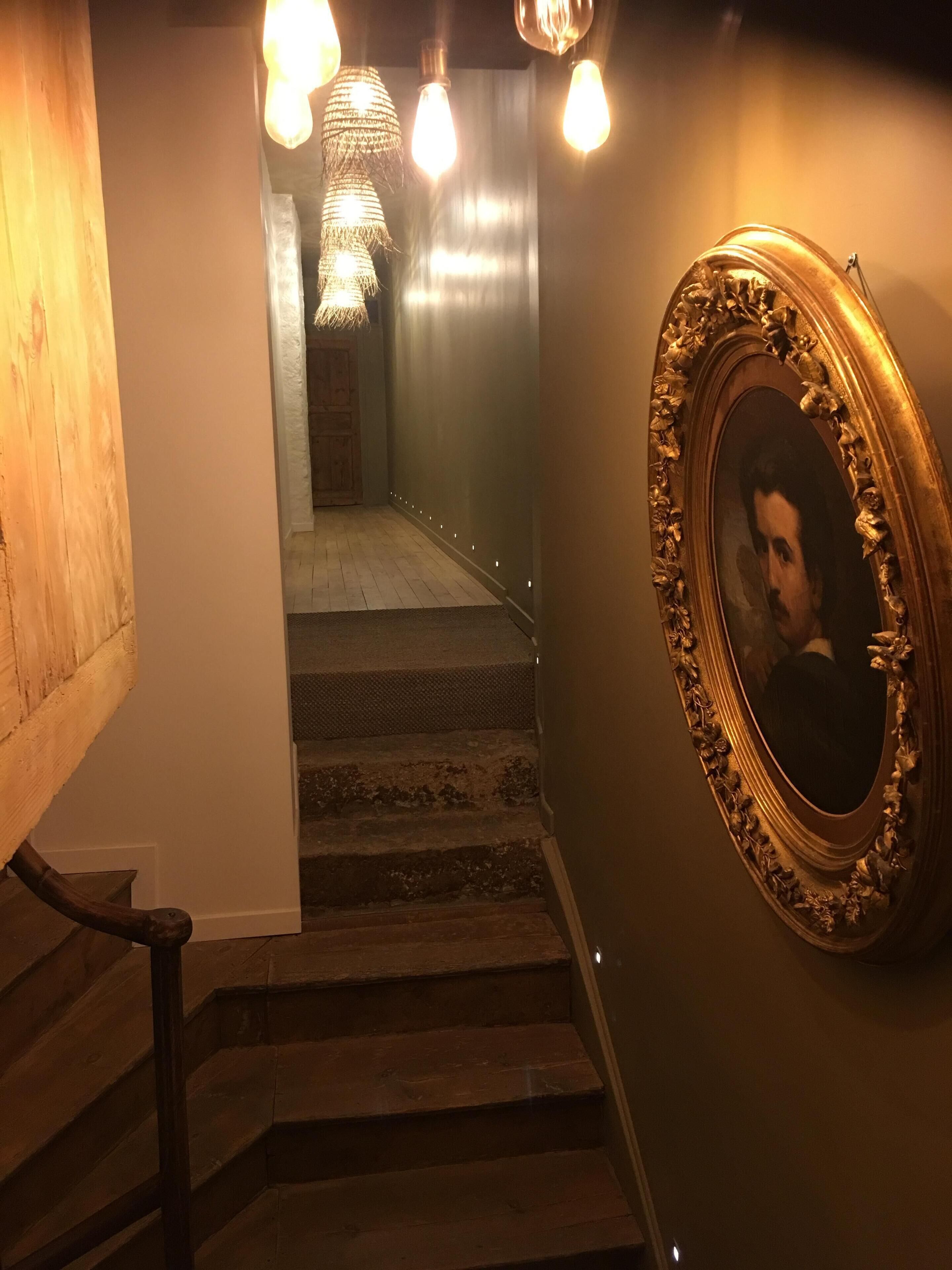 A staircase with a wooden handrail, a wall-mounted picture frame, and a chandelier.