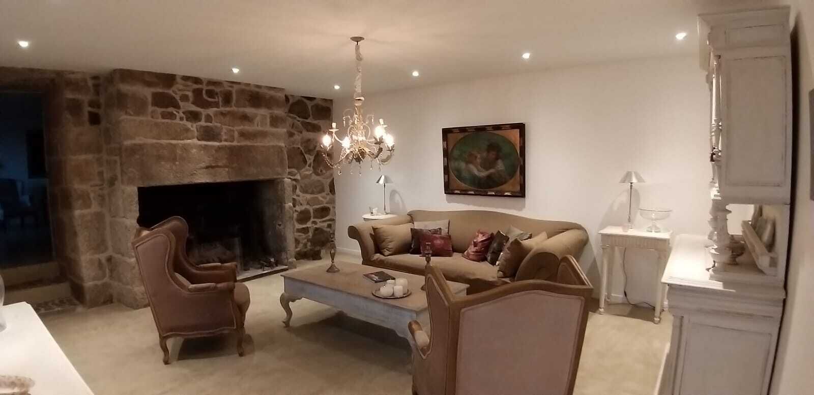Ein gemütliches Wohnzimmer mit Kamin aus Stein, einer Kristallleuchtre und einem beigefarbenen Sofa, sowie einem Gemälde an der Wand.