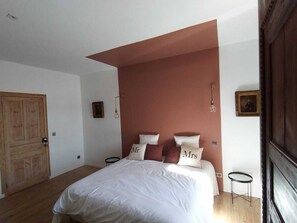 A bedroom with a large bed, a wooden door, a small table, and a picture on the wall.