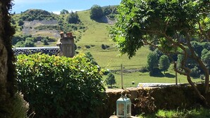 Paisaje rural con un muro de piedra, un farol y vista a un edificio distante.