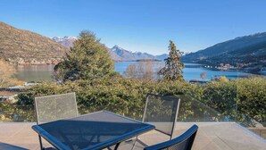 A terrace with two metal chairs and a table overlooking a lake and mountains.