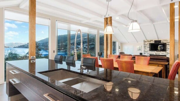A modern kitchen with a large island, a dining area with striped chairs, and a view of a lake and mountains.