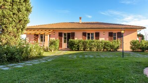 Uma casa de dois andares com telhado de cerâmica, varanda frontal e gramado bem cuidado.