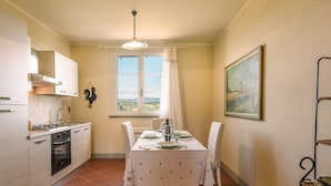 Uma cozinha com uma mesa de jantar posta para quatro pessoas, uma janela com cortinas e um quadro na parede.