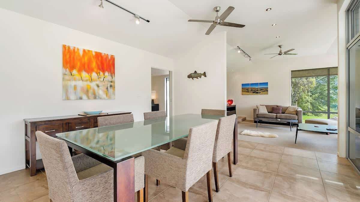 Uma área de jantar moderna com mesa de vidro e cadeiras de fibra natural, um sofá e uma decoração de peixe na parede.