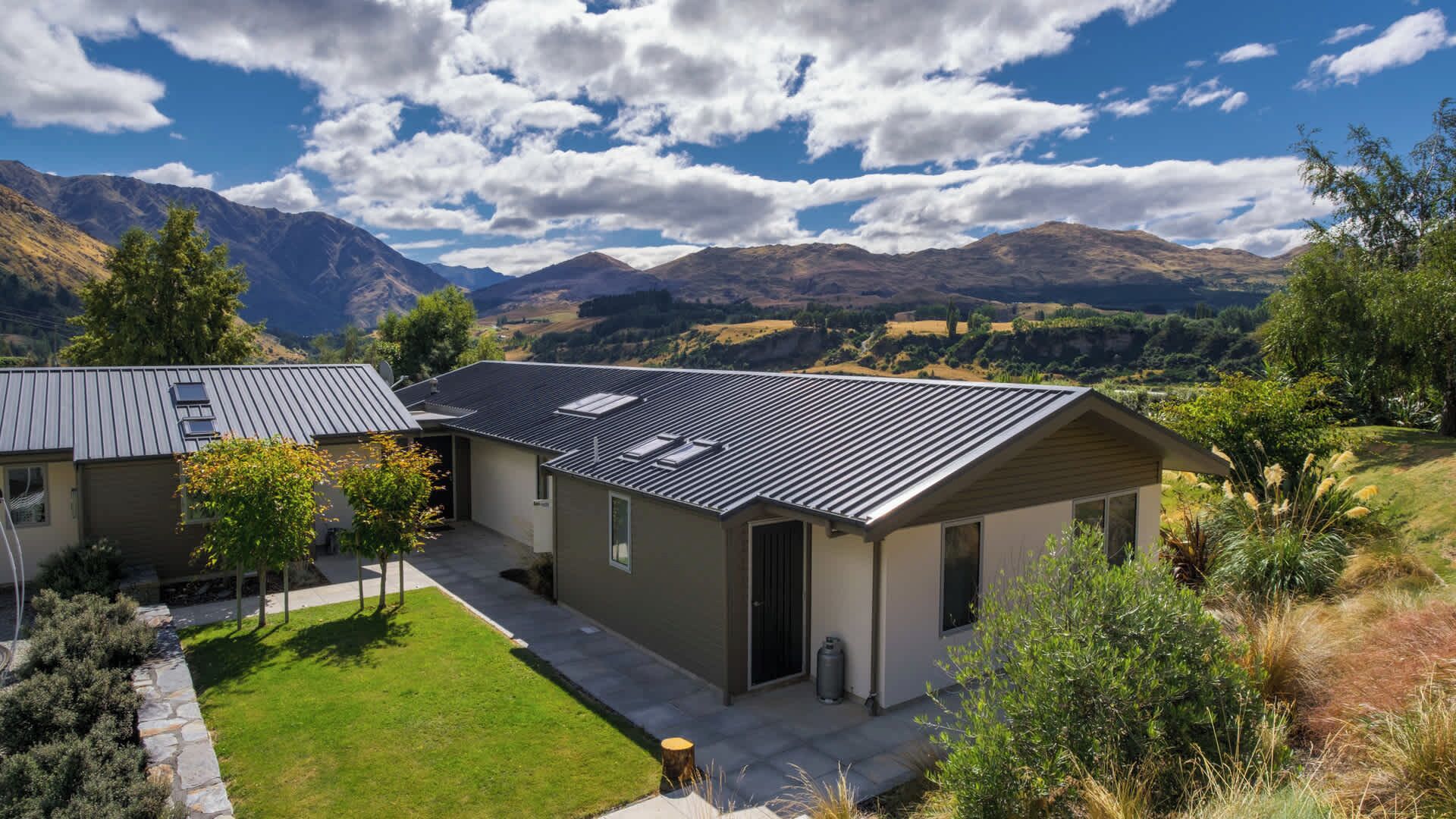 A modern house with a sloped roof, surrounded by a well-maintained lawn and a view of mountains.