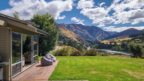Una casa moderna con una puerta de cristal que da a una terraza, con vistas a un río y montañas.