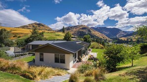 Ein modernes Haus mit geneigtem Dach, umgeben von einem gepflegten Garten und einem malerischen Bergpanorama.