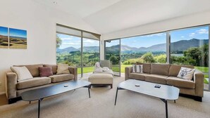 Ein modernes Wohnzimmer mit zwei Sofas, einem Couchtisch und Blick auf eine gebirgige Landschaft durch große Fenster.