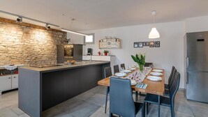A modern kitchen with a stone accent wall, a central island, and a dining area with a wooden table and chairs. - Amazing home in Hreljici (Hreljici)