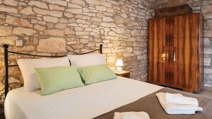A bedroom with a stone wall, a wooden wardrobe, a bed with white and green bedding, and a nightstand with a lamp. - Amazing home in Hreljici (Hreljici)