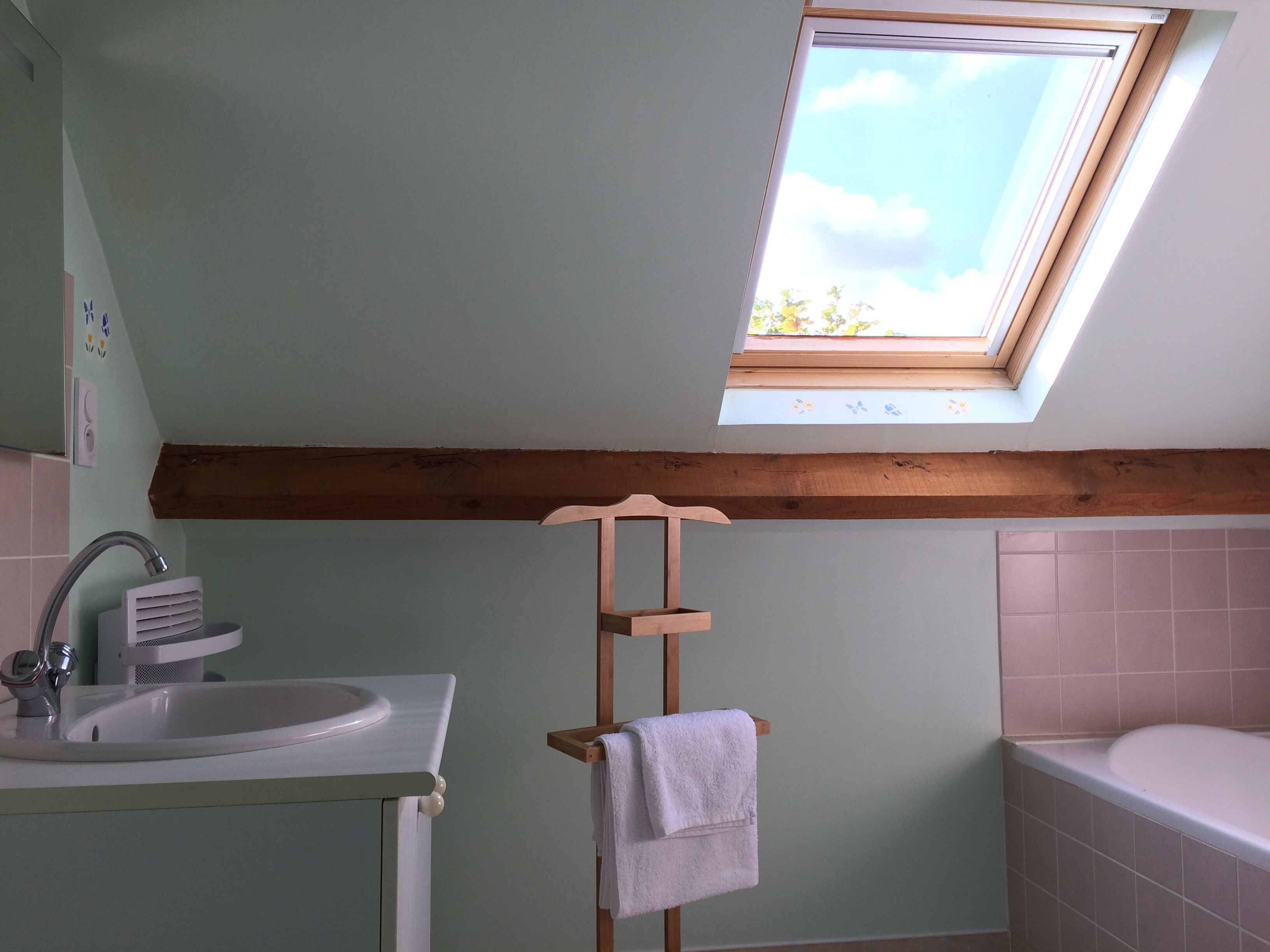 Ein Badezimmer mit Oberlicht, Holzbalkendecke, Waschbecken und Badewanne.