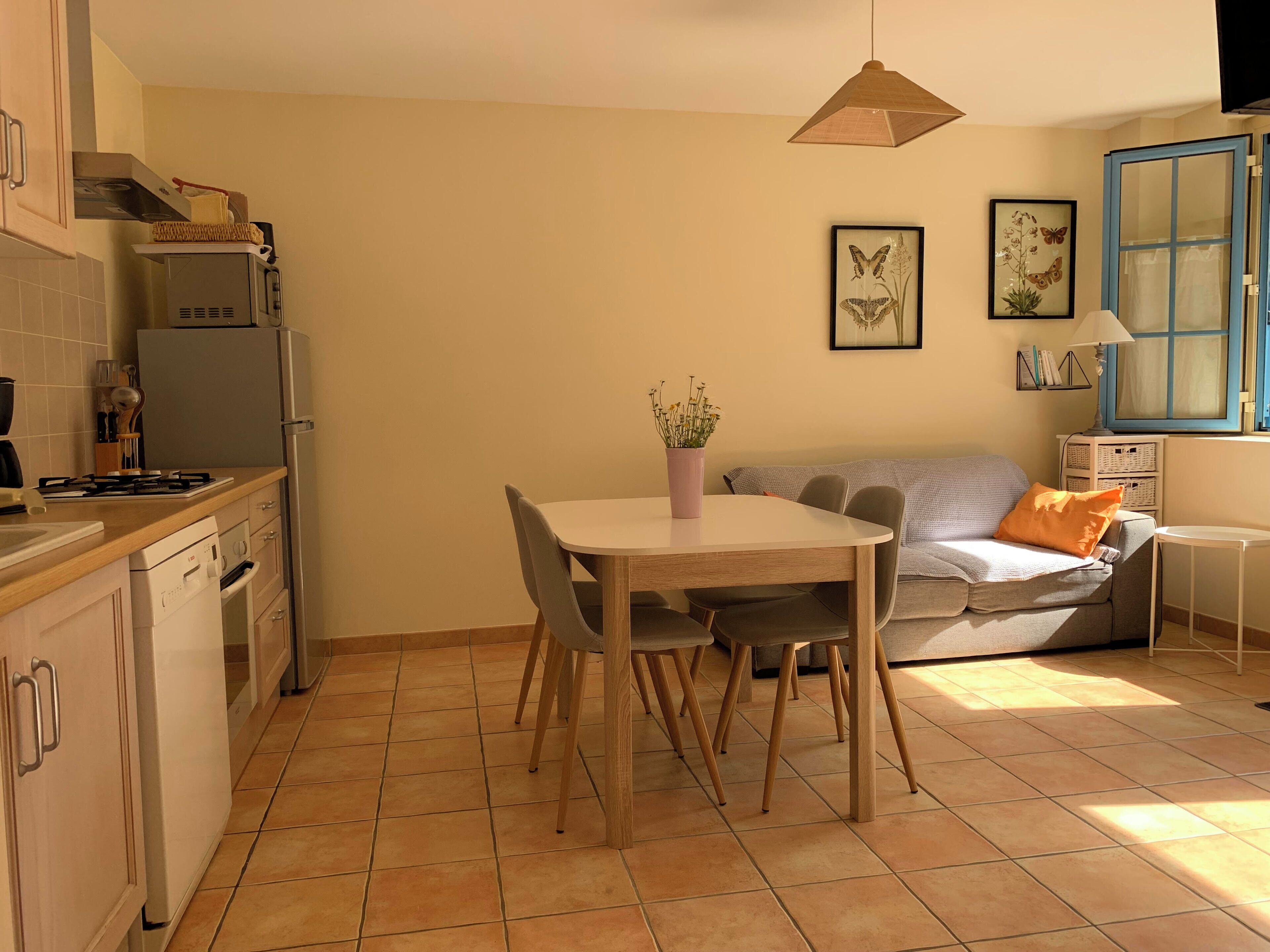 A compact kitchen with a dining area, a sofa, and a window with blue shutters.