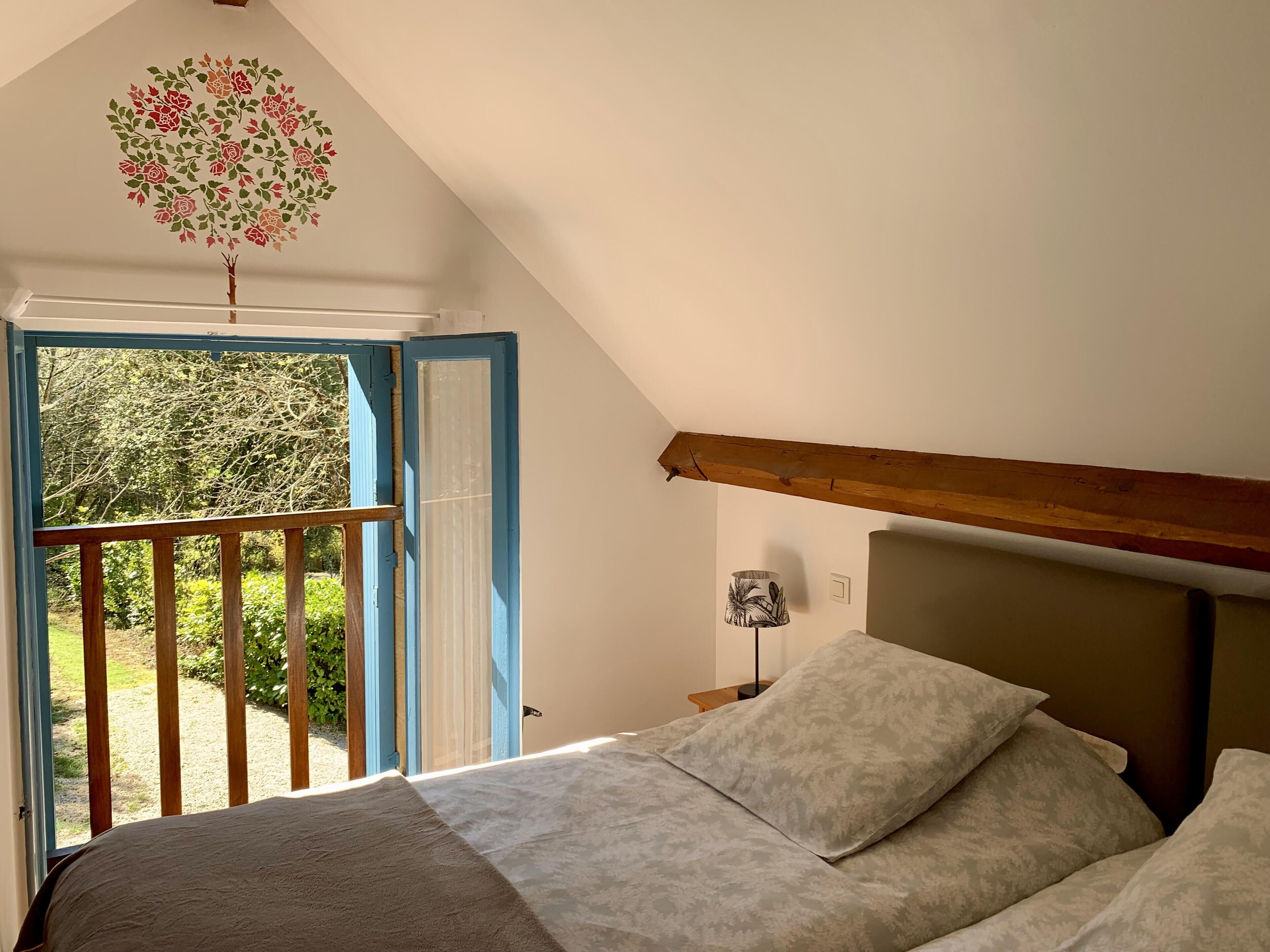 Een slaapkamer met een bed, nachtkastje, lamp en uitzicht op groen.