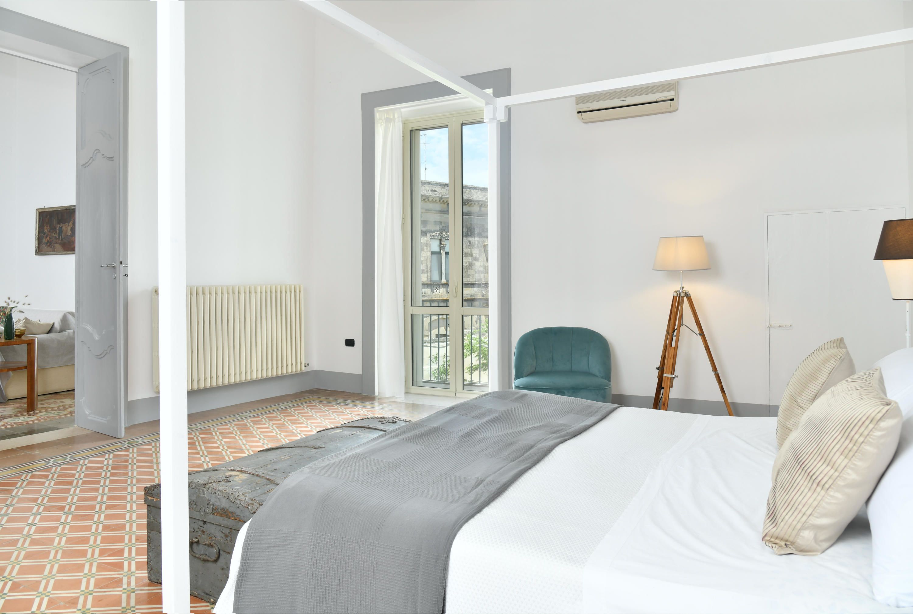 Ein Hotelzimmer mit Bett, einem Sessel, einer Lampe und Blick auf die Stadt durch das Fenster.