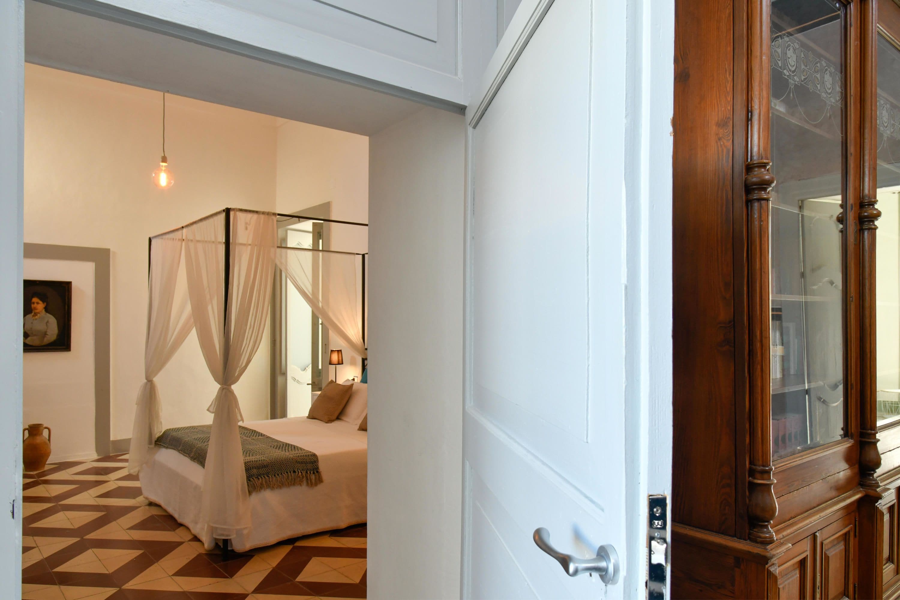 A bedroom with a four-poster bed, a bedside lamp, and a large mirror.