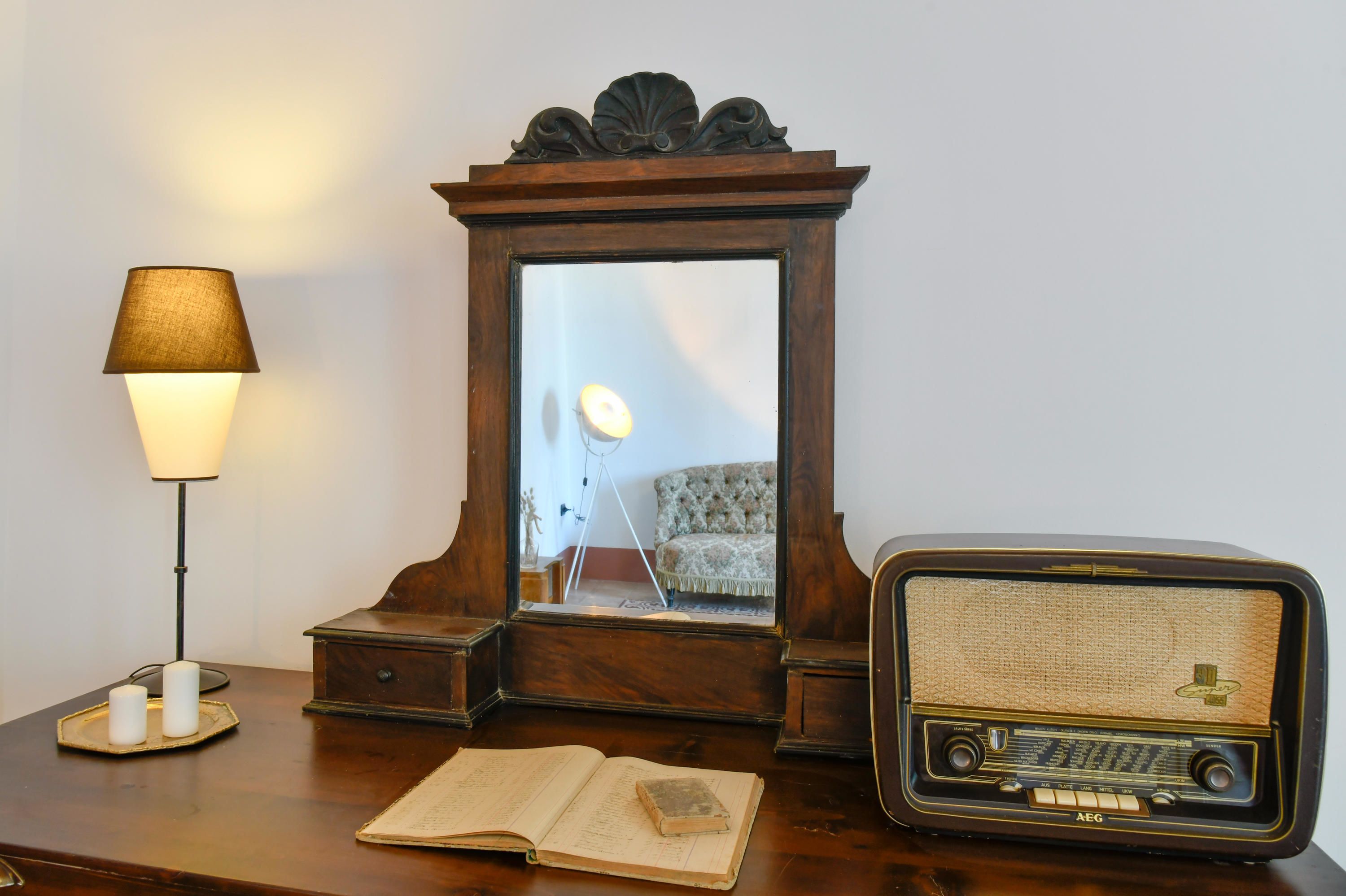 Una mesa de madera con una lámpara, un libro, un espejo y una radio antigua.