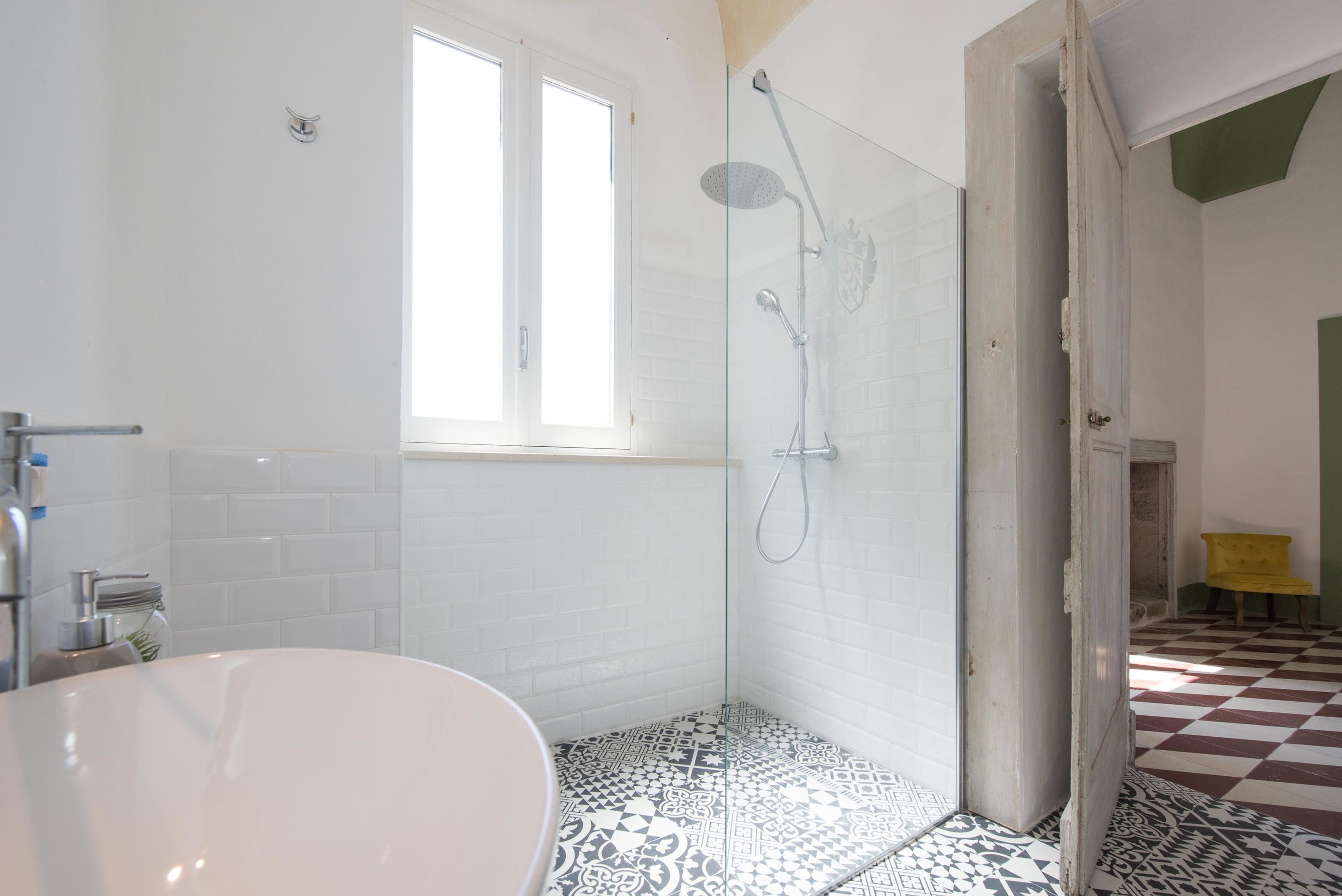 A bathroom with a white bathtub, a glass-enclosed shower, and patterned floor tiles.