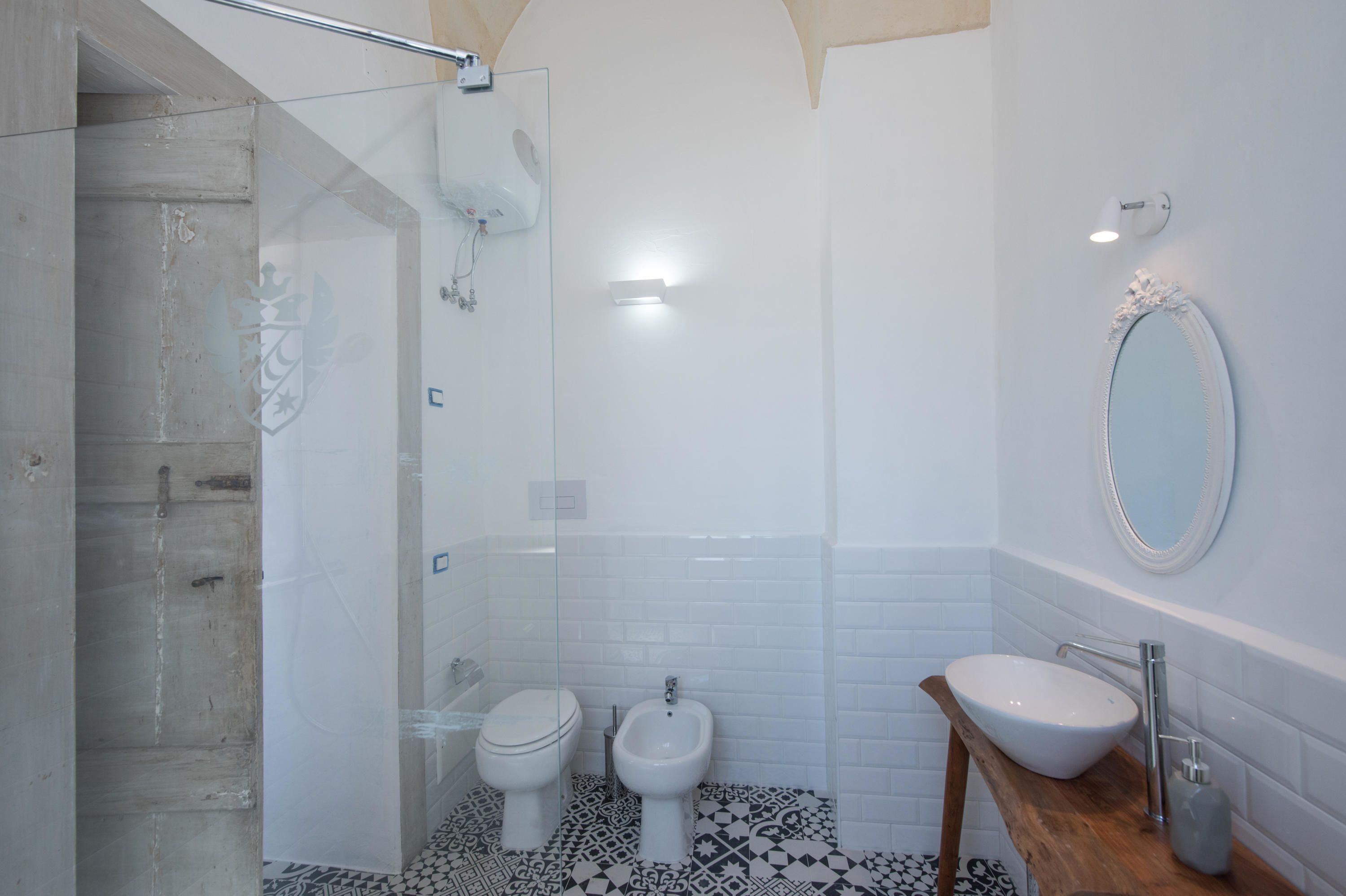 A modern bathroom with a glass shower enclosure, a bidet, a sink with a wooden countertop, and a mirror.