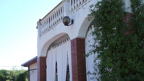 Un edificio con fachada blanca, columnas de ladrillo rojo y un balcón con barandilla blanca.