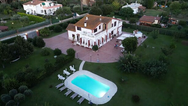 Vista aérea de una amplia casa con piscina, rodeada de céspedes cuidados y árboles.