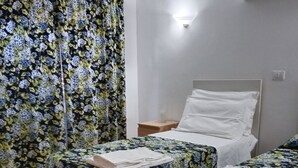 Una habitación con dos camas, cada una con ropa de cama floral, una mesita de noche, un aire acondicionado de pared y una cortina estampada con flores.