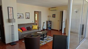 A living room with a sofa, coffee table, and chairs, a bookshelf, and a sliding glass door to the outside.
