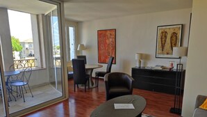 A modern living room with a glass door leading to a balcony, a round table with a chair, a sofa, and a patterned rug.