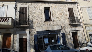 A two-story building with stone walls, a balcony with metal railings, and a visible storefront with signage.