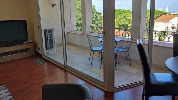 A room with a TV, a sliding glass door leading to an outdoor balcony with chairs and a table.