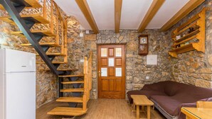 Una habitación acogedora con una escalera de madera, una pared de piedra, una puerta de madera, un sofá marrón y una pequeña mesa de madera.