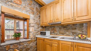 Una cocina con armarios de madera, pared de piedra, microondas y una ventana con planta en maceta.