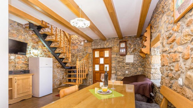 Una cocina acogedora con una mesa de madera, paredes de piedra y una escalera.