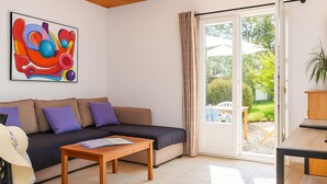 En stue med sofa, sofabord, et billede og en skydedør, der fører til et udendørs område.
