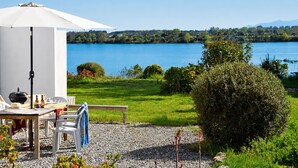 En terrasse med et bord, stole og en parasol med udsigt over en sø.