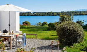 Eine Terrasse mit Tisch, Stühlen und Sonnenschirm mit Blick auf einen See.