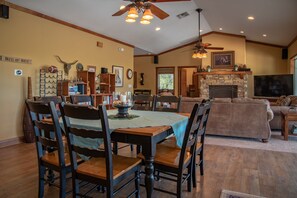 A dining area with a wooden table and chairs, a fireplace, and a living room with a sofa and television.